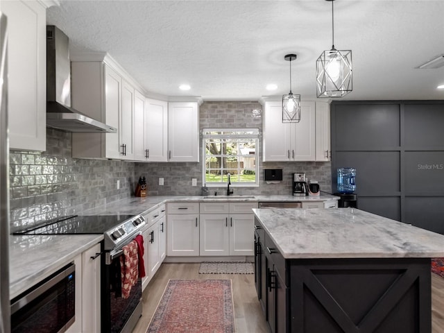 kitchen with stainless steel appliances, wall chimney range hood, a sink, and white cabinetry