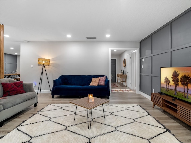 living area with light wood finished floors, visible vents, a decorative wall, and recessed lighting