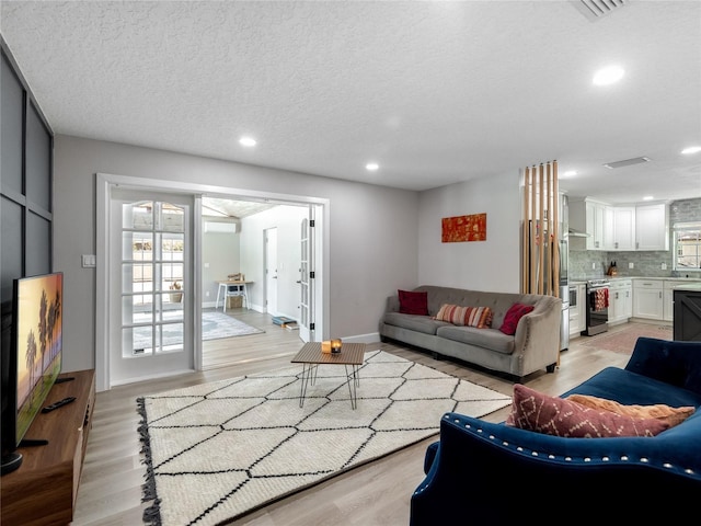 living room with light wood-type flooring, visible vents, a textured ceiling, and recessed lighting