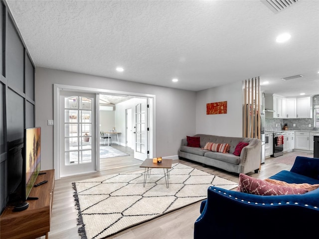 living area with recessed lighting, visible vents, light wood-style flooring, and a textured ceiling