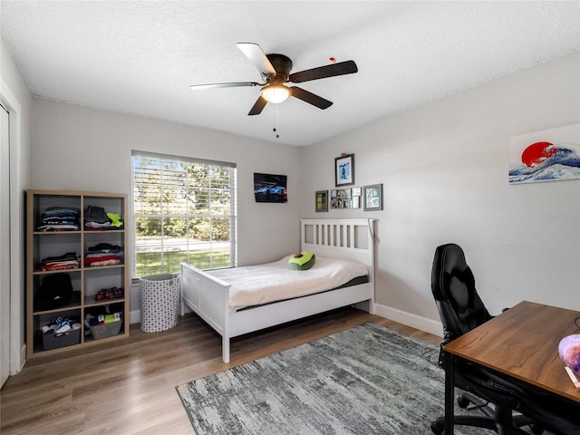 bedroom featuring baseboards, a textured ceiling, a ceiling fan, and wood finished floors