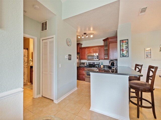 kitchen with a kitchen breakfast bar, stainless steel appliances, kitchen peninsula, track lighting, and light tile flooring