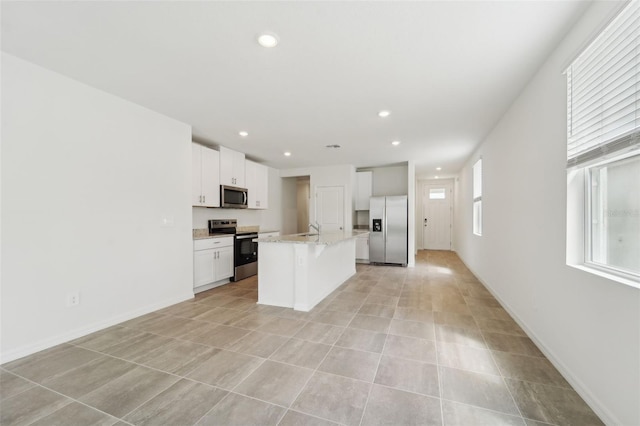 kitchen featuring a kitchen island with sink, appliances with stainless steel finishes, light stone countertops, white cabinets, and sink