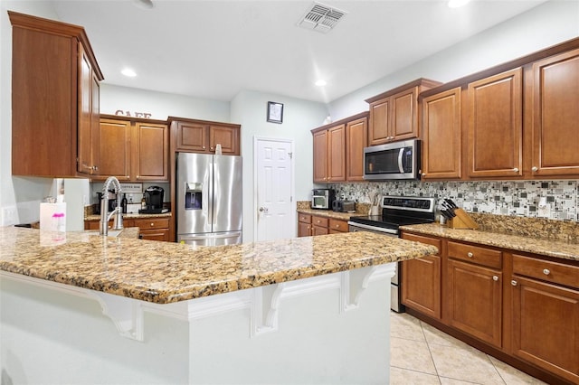 kitchen with light stone countertops, a breakfast bar, backsplash, and appliances with stainless steel finishes