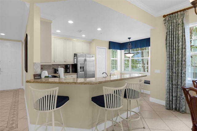 kitchen featuring light tile patterned floors, kitchen peninsula, stainless steel refrigerator with ice dispenser, decorative backsplash, and decorative light fixtures