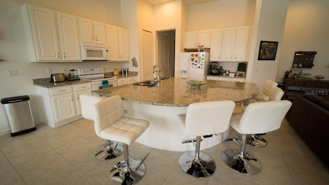 kitchen with sink, light stone counters, white appliances, a breakfast bar area, and a center island with sink