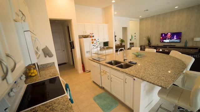 kitchen with white appliances, a center island with sink, sink, light stone countertops, and a breakfast bar area