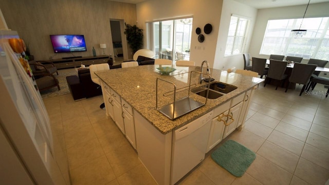 kitchen with light stone counters, sink, light tile patterned floors, a center island with sink, and hanging light fixtures