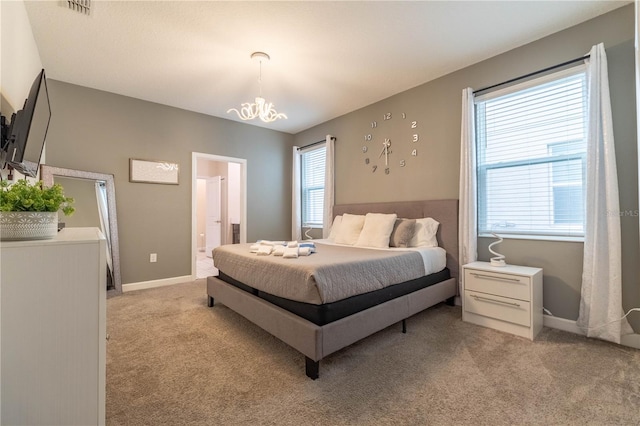 carpeted bedroom featuring multiple windows, ensuite bath, and a notable chandelier