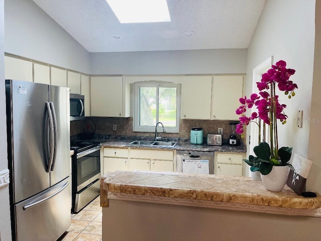 kitchen with appliances with stainless steel finishes, backsplash, vaulted ceiling with skylight, sink, and light tile floors