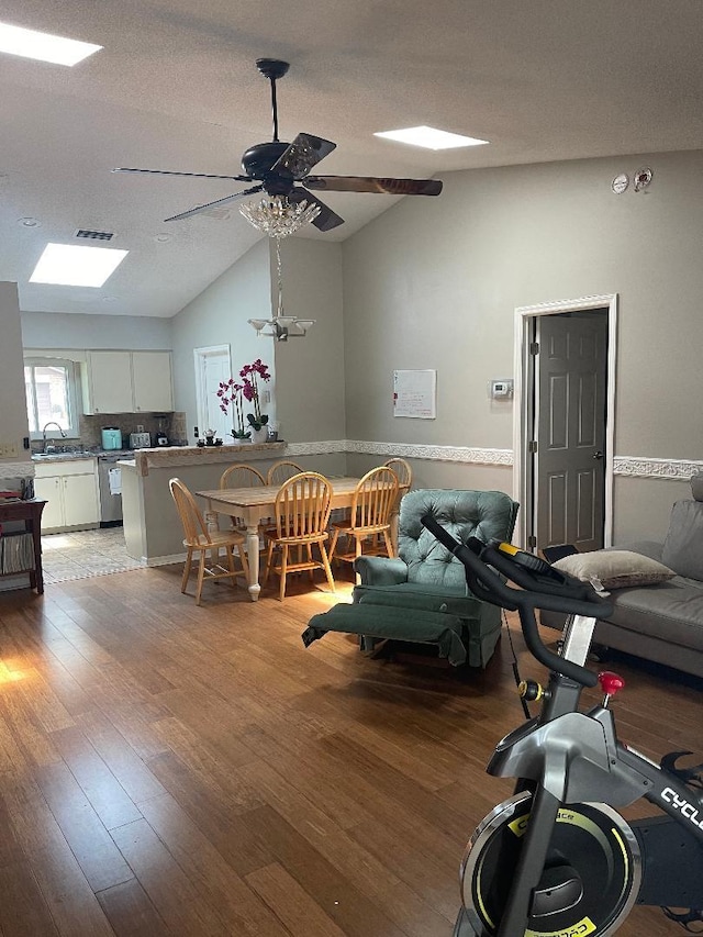 interior space with a textured ceiling, hardwood / wood-style flooring, vaulted ceiling with skylight, sink, and ceiling fan