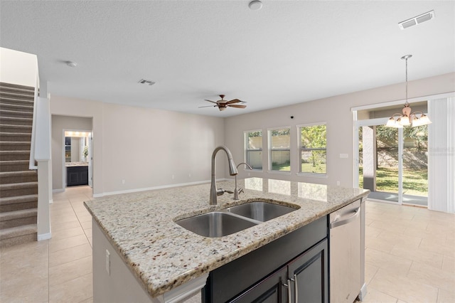 kitchen with an island with sink, decorative light fixtures, stainless steel dishwasher, light stone counters, and sink