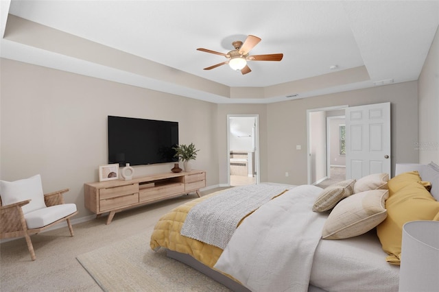 bedroom with ceiling fan, connected bathroom, a tray ceiling, and carpet floors