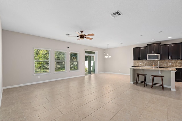 unfurnished living room featuring light tile patterned flooring and ceiling fan with notable chandelier