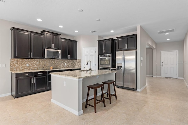 kitchen featuring a center island with sink, sink, light stone countertops, a kitchen breakfast bar, and stainless steel appliances