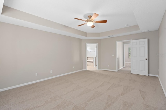 empty room with ceiling fan, light colored carpet, and a tray ceiling