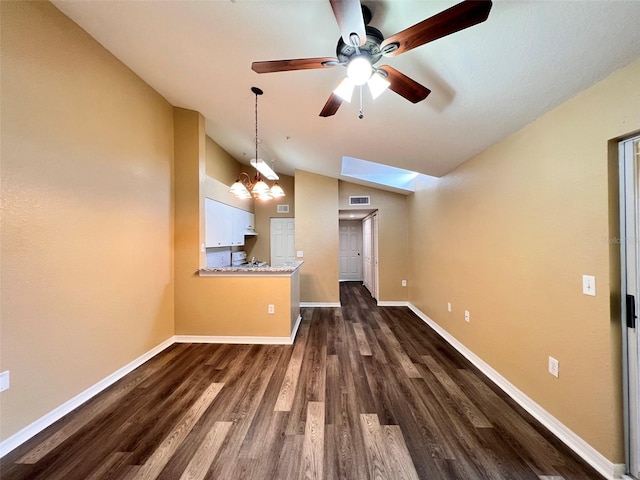 unfurnished living room featuring dark wood-type flooring, vaulted ceiling with skylight, and ceiling fan with notable chandelier