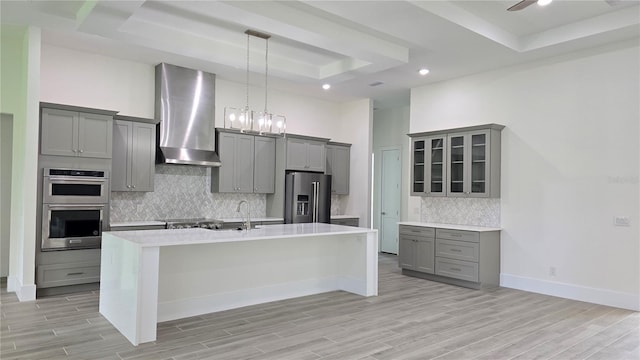 kitchen featuring gray cabinets, wall chimney range hood, stainless steel appliances, and a tray ceiling