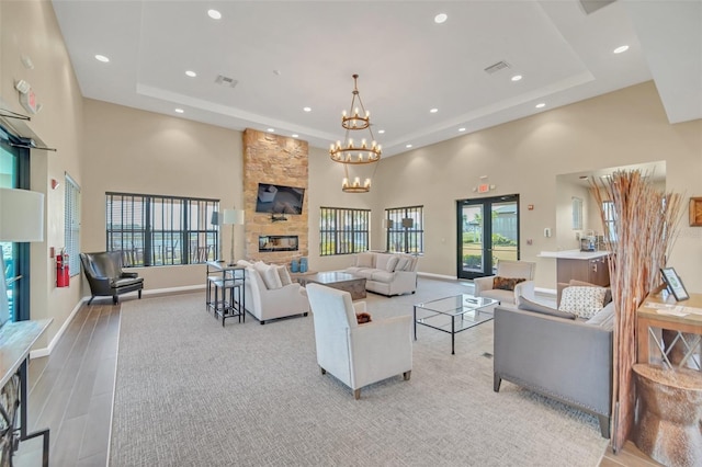 living room featuring french doors, a fireplace, an inviting chandelier, a high ceiling, and a raised ceiling