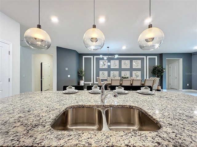 kitchen featuring light stone counters, sink, and decorative light fixtures