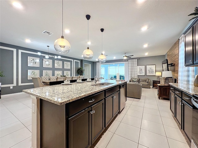 kitchen with ceiling fan, sink, light stone counters, decorative light fixtures, and a kitchen island with sink