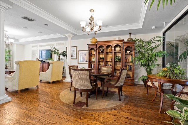 dining area with a raised ceiling, ornamental molding, ornate columns, wood-type flooring, and a chandelier