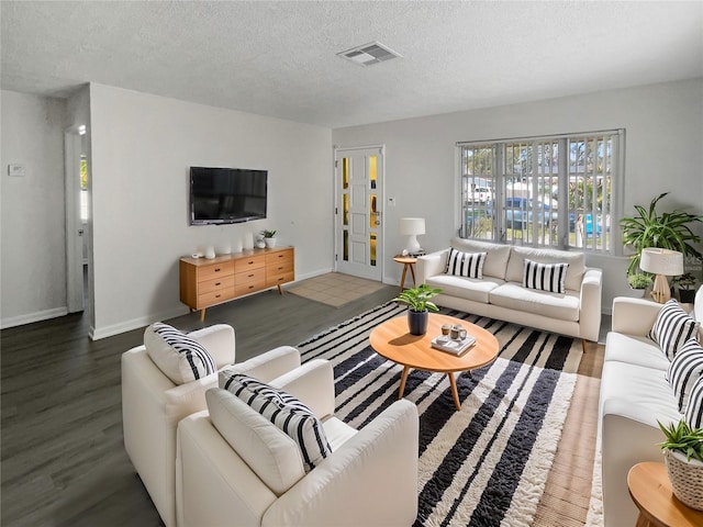 living area with a textured ceiling, wood finished floors, visible vents, and baseboards