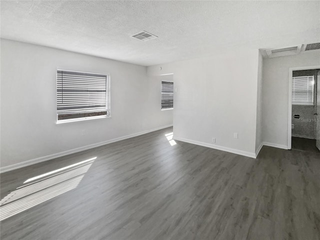 unfurnished room featuring dark wood-style flooring, visible vents, a textured ceiling, and baseboards