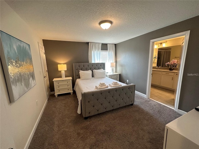 bedroom with dark colored carpet, ensuite bathroom, a sink, a textured ceiling, and baseboards