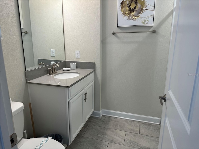 bathroom featuring a textured wall, toilet, vanity, baseboards, and tile patterned floors