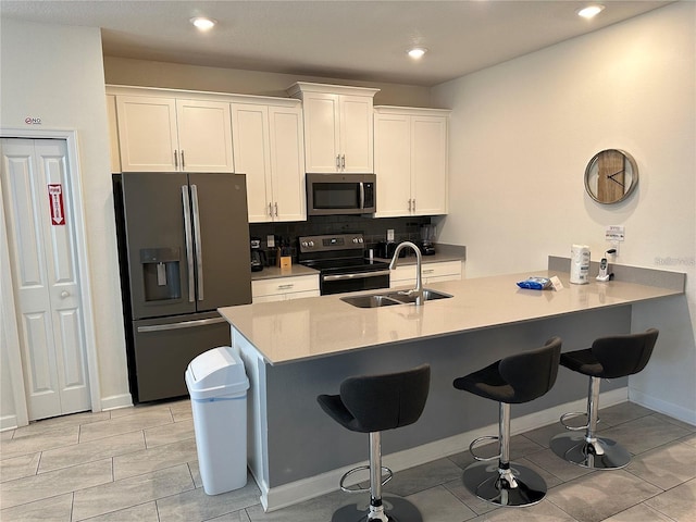 kitchen with stainless steel appliances, a peninsula, a sink, white cabinetry, and light countertops