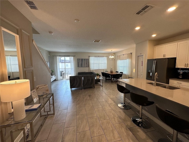 kitchen with a sink, visible vents, white cabinetry, light countertops, and black fridge