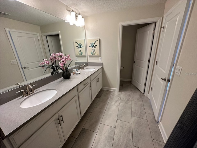 bathroom featuring double vanity, a textured ceiling, visible vents, and a sink