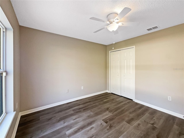 unfurnished bedroom with ceiling fan, a closet, dark wood-type flooring, and a textured ceiling