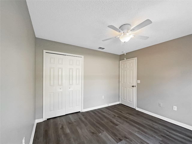 unfurnished bedroom with ceiling fan, a closet, dark wood-type flooring, and a textured ceiling