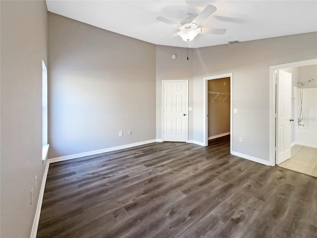 unfurnished bedroom with ceiling fan, a spacious closet, dark wood-type flooring, ensuite bathroom, and a closet