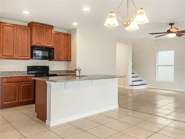 kitchen with light tile patterned flooring, an island with sink, black appliances, and decorative light fixtures