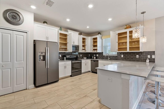 kitchen featuring decorative light fixtures, white cabinets, a kitchen breakfast bar, kitchen peninsula, and stainless steel appliances