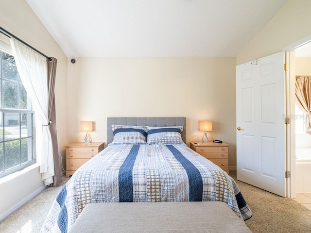 carpeted bedroom featuring lofted ceiling and ensuite bath