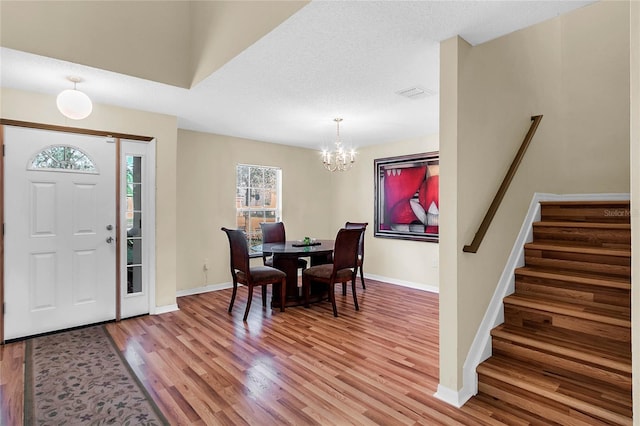 foyer entrance with light hardwood / wood-style floors, a textured ceiling, and a chandelier