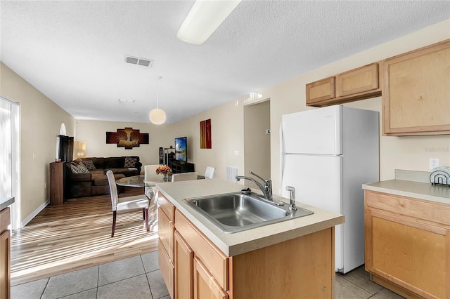 kitchen featuring sink, white fridge, light tile patterned floors, an island with sink, and light brown cabinetry