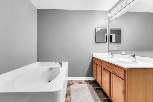 bathroom with a textured ceiling, vanity, and tiled bath