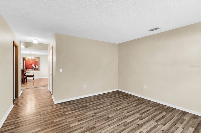 unfurnished room with a textured ceiling, an inviting chandelier, and hardwood / wood-style flooring