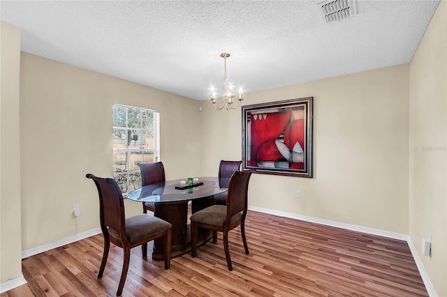 dining area with a textured ceiling, a chandelier, and hardwood / wood-style flooring