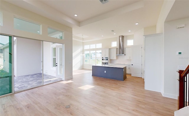 kitchen featuring white cabinets, light wood-type flooring, a kitchen island, and wall chimney exhaust hood