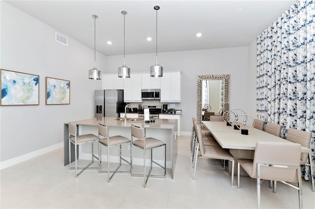 kitchen featuring a breakfast bar area, white cabinets, stainless steel appliances, an island with sink, and light tile patterned flooring