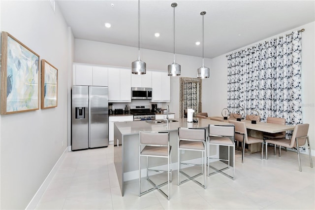 kitchen featuring white cabinets, a kitchen island with sink, appliances with stainless steel finishes, pendant lighting, and sink