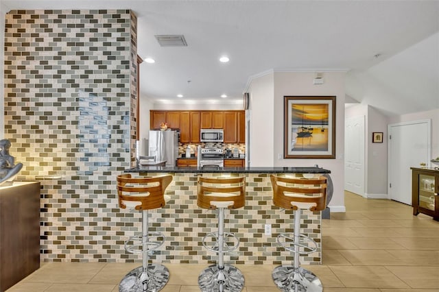 kitchen with a breakfast bar area, crown molding, kitchen peninsula, stainless steel appliances, and decorative backsplash