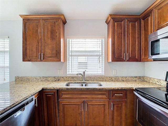 kitchen with appliances with stainless steel finishes, light stone counters, and sink