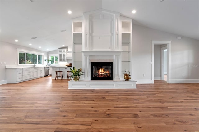 unfurnished living room featuring sink, a high end fireplace, vaulted ceiling, and light wood-type flooring